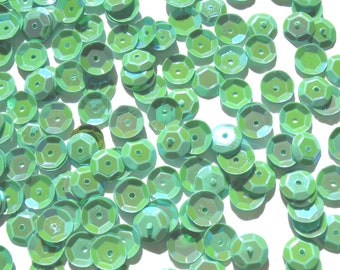 May include: A scattering of light green iridescent sequins, each with a slightly raised, faceted surface.