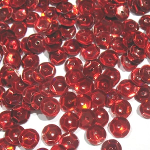 Peut inclure: Une dispersion de sequins rouges brillants. Chaque sequin est de forme hexagonale plate avec un trou central. Les sequins ont une surface réfléchissante, captant la lumière et créant un effet scintillant. Idéal pour les projets d'artisanat.