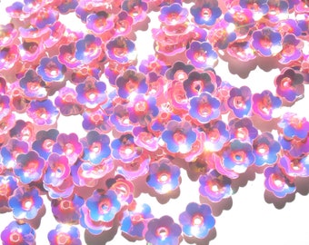 Könnte beinhalten: Eine Streuung von schimmernden, pinkfarbenen und blauen Blüten-Pailletten. Die Pailletten haben einen holografischen Schimmer und sind perfekt zum Basteln und Verzieren von Projekten.