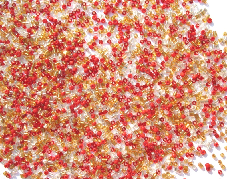 May include: A close-up image of a large quantity of small, round, glass beads. The beads are a mix of red and gold colors.