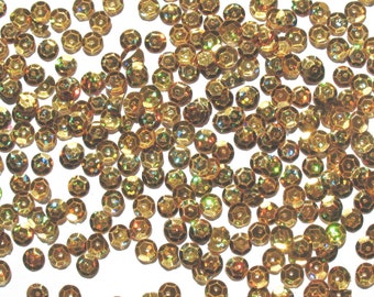Könnte beinhalten: Eine große Menge an goldenen, schimmernden Pailletten, die auf einem weißen Hintergrund verstreut sind.