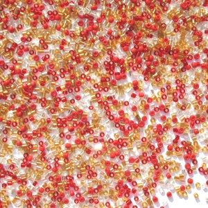 May include: A mix of red, gold, and clear glass seed beads. The beads are small and round, and they are scattered on a white background.