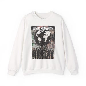 May include: White long-sleeved sweatshirt with a graphic print of a globe with roots and people holding hands. The text "ONE HUMANITY" is printed above the globe.