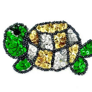 May include: A turtle-shaped patch crafted with vibrant green, metallic gold, and silver sequins. The outline and details are defined by small, dark grey beads, creating a textured surface that forms the head, shell, and flippers of the sea creature.