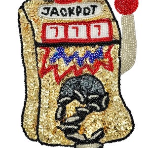 May include: A gold sequined slot machine with the word "JACKPOT" at the top. The machine features red, white, and blue accents, with the lucky number 7 displayed. A red beaded ball sits atop the machine, and another is on the side.