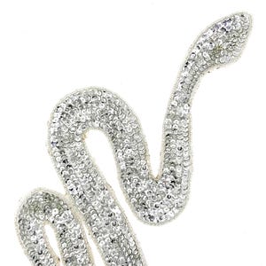 May include: A silver sequined snake applique. The snake is curled in an S shape with its head raised.
