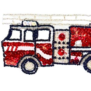 May include: A decorative fire truck design, featuring red sequins and white accents, outlined with black and silver beads. The fire truck has a ladder on top and is set against a white background. The design is likely for an applique or patch.