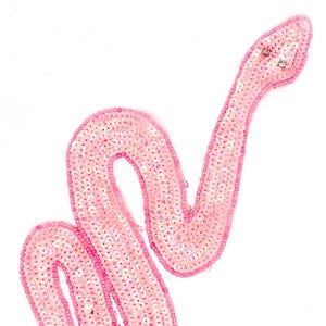 May include: Pink sequined snake applique patch. This patch is ideal for adding a touch of sparkle to your clothing or accessories.