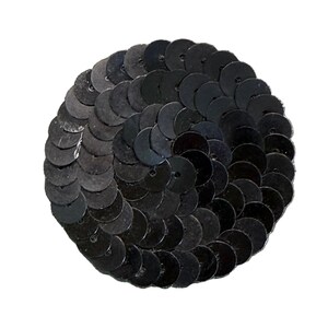May include: A circular patch composed of overlapping black sequins arranged in a spiral pattern. Each individual sequin is round with a small center hole, creating a textured, reflective surface that forms a solid, uniform black disc shape.