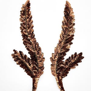 May include: A pair of symmetrical leaf-shaped appliques covered in metallic copper-colored sequins. Each piece features a central stem with two branching fronds, densely embroidered with shimmering, reflective circular sequins in a warm bronze tone.