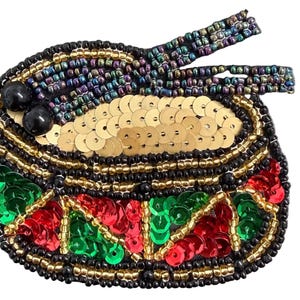 May include: A beaded patch shaped like a bowl of ramen, featuring gold sequins for noodles, two black beads, and iridescent blue beads for chopsticks. The bowl is decorated with red and green sequins, outlined in black and gold seed beads.
