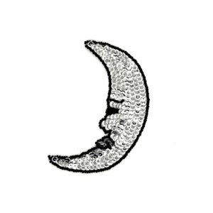 May include: A crescent moon patch with a smiling face, made of silver sequins and outlined in black. The patch is on a white background, creating a striking contrast.