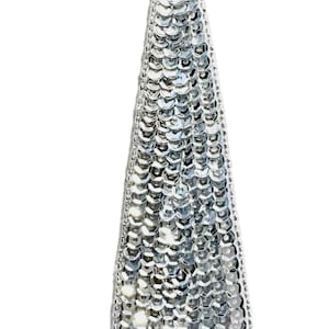 May include: A silver sequined teardrop-shaped ornament. The ornament is covered in small, shiny, silver sequins. The sequins are arranged in neat rows, creating a textured surface. The ornament has a pointed top and a rounded bottom.