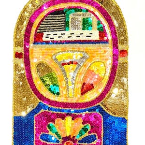 May include: A decorative patch featuring a jukebox design crafted with vibrant sequins in gold, hot pink, blue, purple, green, yellow, and orange. The arched top contains a black and white record player detail, while the base displays a colorful floral motif.