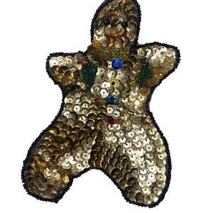 May include: A gold sequined gingerbread man ornament with black bead accents and colorful details.