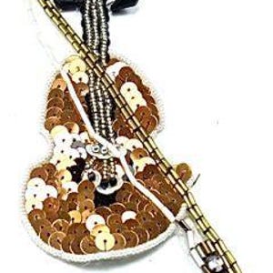 May include: A gold sequined violin applique with a black bow and a gold bow on the neck. The violin has a white background and a gold bow on the neck. The violin is attached to a gold string.