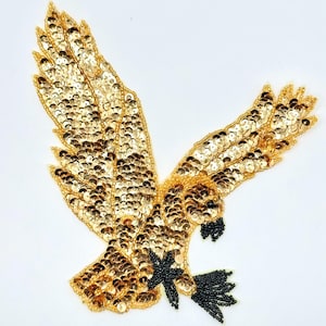 May include: A gold sequined eagle applique with black beaded accents. The eagle is in flight with its wings spread wide.