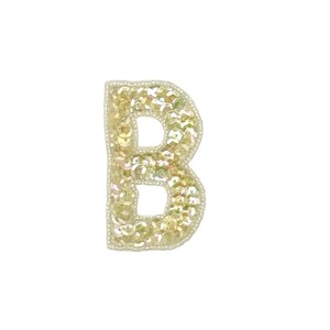 May include: A sequined letter "B" patch in a light gold color. The patch is outlined with small, off-white beads. The sequins have a shimmering, iridescent quality, reflecting light. The letter is isolated on a white background.