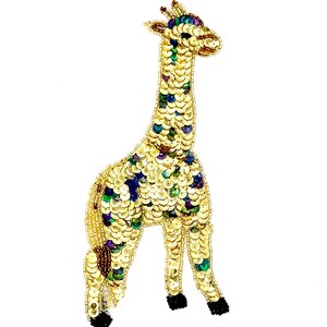 May include: A giraffe-shaped patch crafted from gold, green, and purple sequins. The design features a long neck, a small head with tiny ears, and four legs ending in black beaded hooves. The body is covered in overlapping metallic sequins.