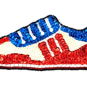 May include: A sneaker-shaped patch crafted from vibrant red, white, and blue sequins. The design features a red toe and heel, a white midsection, and blue eyelet detailing. The entire perimeter is outlined with small black beads for definition.