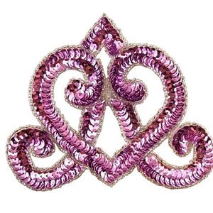 May include: A decorative tiara in a heart-shaped design, covered in pink sequins. The tiara has a silver beaded border and is set against a white background. The design is symmetrical and ornate, suitable for embellishing clothing or accessories.