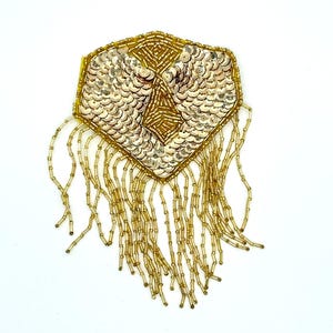 May include: A gold sequin and beaded embellishment with a geometric design. The central section features a diamond pattern, while the outer edges are adorned with gold sequins. Long beaded fringe hangs from the bottom, creating a decorative accessory.