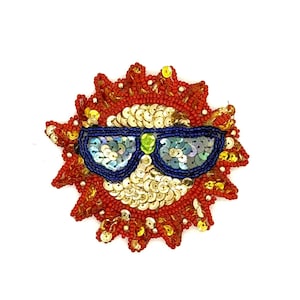 May include: A beaded sunburst design with sunglasses. The sun's rays are red with gold sequins and red beads. The sunglasses are blue with iridescent sequins and a green accent.