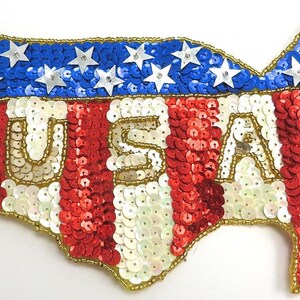 May include: A red, white, and blue sequined patch in the shape of the United States with the word "USA" spelled out in gold sequins.