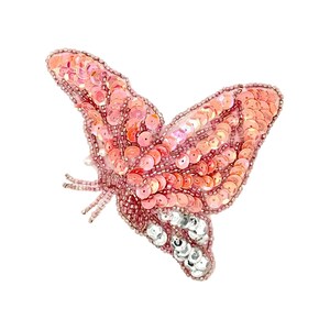 May include: A pink sequined butterfly brooch with a detailed design. The butterfly has a gradient of pink sequins, with silver sequins on the lower wings. The brooch is set against a white background.