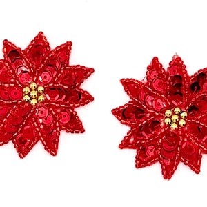 May include: Two red poinsettia flower embellishments with gold sequin centers. The flowers are made of sequins and are perfect for adding a festive touch to crafts and projects.