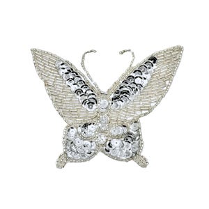 May include: A silver butterfly-shaped embellishment with intricate detailing. The wings are adorned with rows of small, shiny sequins and beads, creating a textured and reflective surface. The butterfly's body is also embellished with sequins.