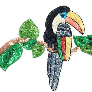 May include: A toucan bird with a long yellow beak, green leaves, and a brown branch, all made of sequins. The toucan is black, blue, green, yellow, and red.
