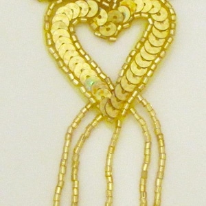 May include: Gold sequined fleur-de-lis with a heart shape and dangling beads.