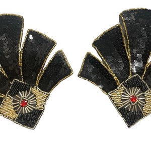 May include: Pair of black sequined fan-shaped embellishments with gold and silver beaded accents. Each has a central square design with a red jewel. Decorative elements for clothing or accessories.