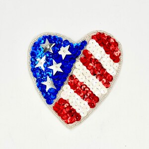 May include: Heart-shaped sequin patch in red, white, and blue, resembling the American flag. The left side features blue sequins with silver stars, while the right side has red and white stripes. The patch is outlined with silver beads.