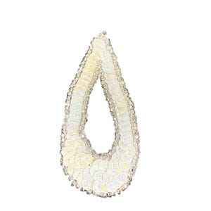 May include: A teardrop-shaped earring with a white sequin design. The earring is outlined with small, clear beads. The sequins have an iridescent quality, reflecting light. The earring is a fashion accessory.