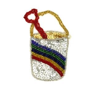 Peut inclure: Un seau de plage en perles avec une pelle rouge. Le seau est argenté avec un motif arc-en-ciel de perles rouges, jaunes, vertes et bleues. La poignée et le bord sont dorés, et la pelle est rouge.