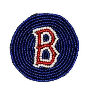 May include: A circular patch featuring a dark blue beaded background with a central letter B. The letter B is outlined in white beads with a red beaded interior. The entire piece is constructed from small, uniform glass beads arranged in rows.