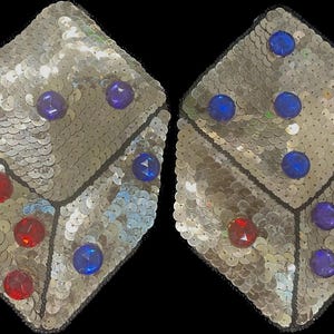 Peut inclure: Deux dés en sequins argentés avec des joyaux rouges et bleus. Les dés sont cousus ensemble et mesurent environ 7,5 cm de diamètre.