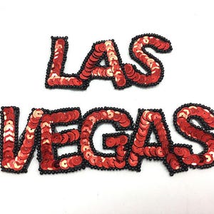 May include: Red sequin letters spelling out "LAS VEGAS" with black thread outlining each letter.