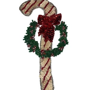 May include: A beaded Christmas ornament featuring a candy cane with red and white stripes and a green wreath with a red bow.