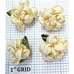 May include: Four off-white satin ribbon flowers with green leaves. Each flower is approximately 1 inch in diameter. The flowers are arranged on a grid background with a 1 inch grid.