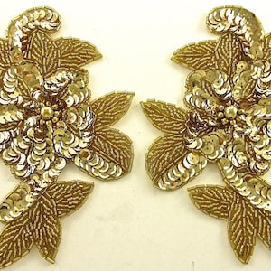 May include: Two gold sequined floral appliques with leaves. The appliques are made of gold sequins and beads and have a delicate, feminine design.