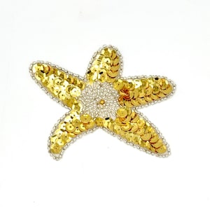 May include: A five-pointed starfish applique featuring gold-colored sequins covering the arms and a central section embellished with small white seed beads. The entire outer edge of the starfish is outlined with a border of tiny silver-colored beads.