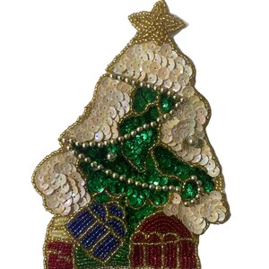 May include: A decorative patch shaped like a Christmas tree, featuring green sequins for the tree, white iridescent sequins for snow, and a gold beaded star topper. The base includes small beaded gift boxes in red and blue colors.