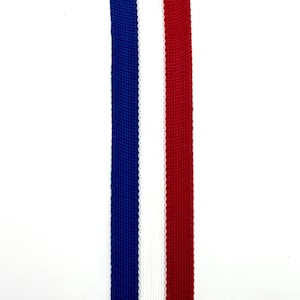 May include: A close-up of a red, white and blue ribbon. The ribbon is made of woven fabric and has a textured surface.