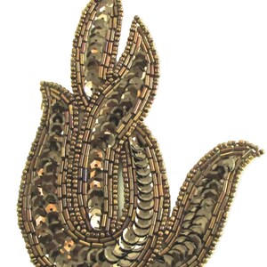 May include: A decorative, abstract floral applique in shades of gold and bronze. The design is embellished with sequins and small beads, creating a textured and shimmering effect. The applique is likely for clothing or accessories.