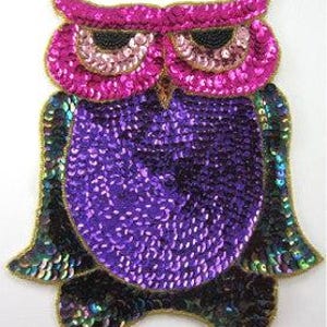 May include: An owl-shaped patch covered in sequins. The owl features bright pink sequins around the eyes, a deep purple sequined body, and dark iridescent black and green sequins on the wings and feet. The entire design is outlined in gold thread.