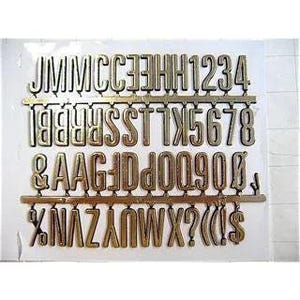 May include: A set of gold-colored, plastic alphabet letters, numbers, and symbols on a plastic grid. The letters are in a serif font and include uppercase letters, numbers 1-0, and various symbols like the ampersand, question mark, and dollar sign.