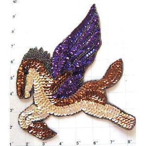 May include: A sequined Pegasus patch featuring a purple wing and a body with brown, copper, and cream-colored sequins. The patch is positioned against a grid background with markings in inches, showing a height of approximately 7 inches.
